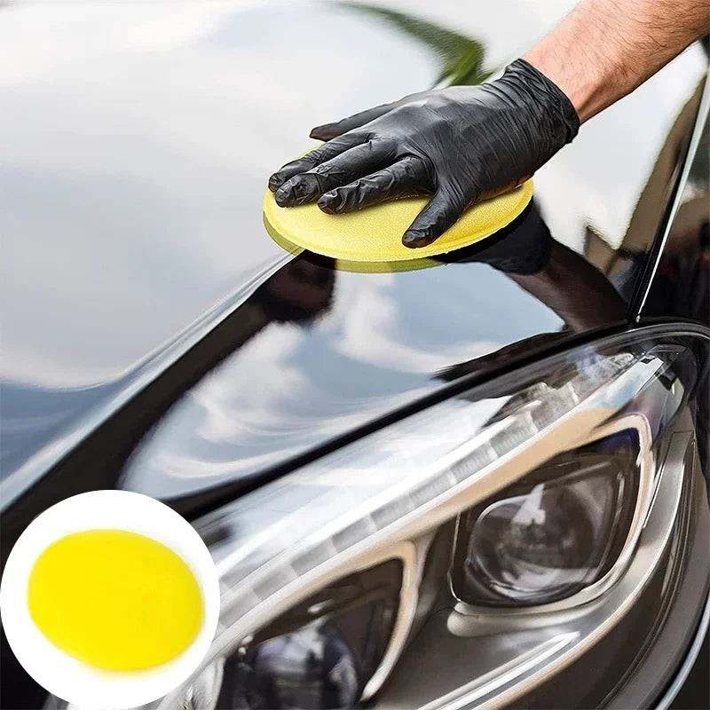 Main gantée appliquant de la cire sur une carrosserie noire avec une éponge Veloria jaune haute densité
